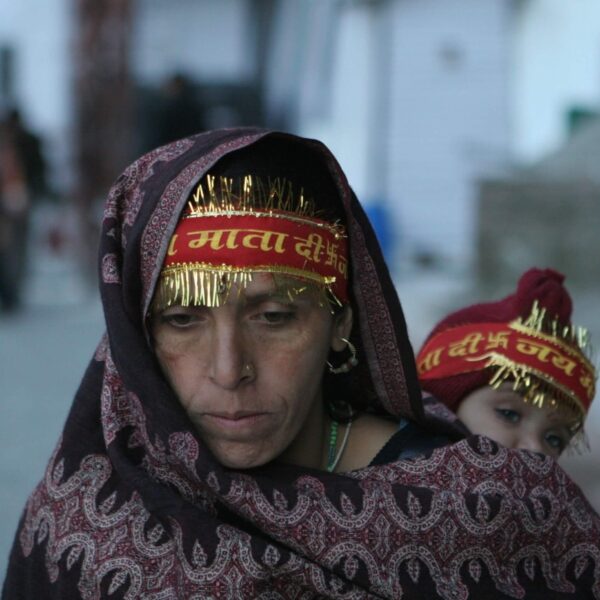 A mother carrying her baby on her back and trekking on a paved path towards the Mata Vaishno Devi Bhawan.