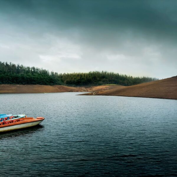 A scenic view of Pykara Lake, a popular tourist attraction in Ooty, Tamil Nadu, with green hills and blue sky in the background.