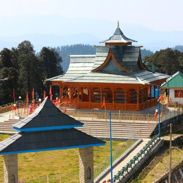 A stunning view of Hatu Peak Temple in Shimla, Himachal Pradesh, surrounded by lush greenery and scenic Himalayan mountains, showcasing traditional wooden architecture.